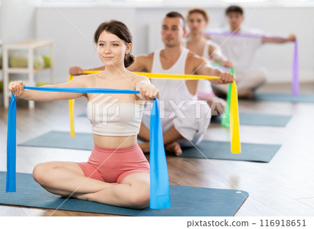 Young girl doing arm workout with band sitting cross-legged Young girl doing arm workout with band sitting cross-legged 116918651