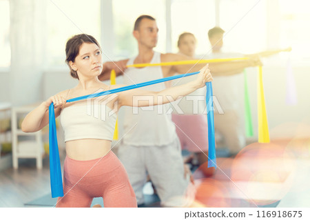 Young girl doing arm workout with resistance band standing on knees 116918675