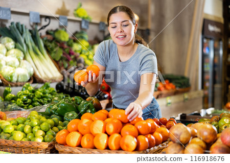 Young woman buyer chooses tangerines in shop Young woman buyer chooses tangerines in shop 116918676