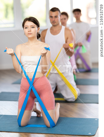 Young girl doing arm workout with resistance band standing on knees 116918789