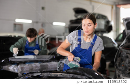 Young female mechanic polishes car with machine 116918802