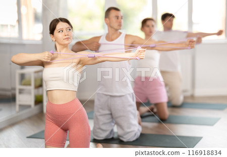 Young girl doing arm workout with resistance band standing on knees 116918834