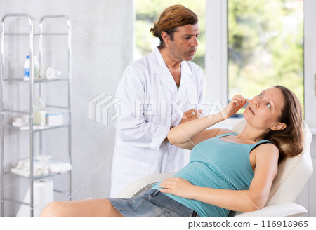 Adult male doctor examining face of female patient 116918965