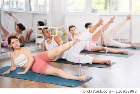 Young men and women practicing leg lift with band on feet lying on the side 116918998