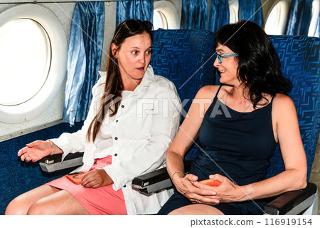 Two beautiful women passengers talking with each other, sitting in the airplane cabin 116919154