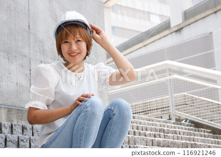 一位戴著頭盔的女士微笑著，背景是一座混凝土建築和樓梯 116921246