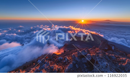 A sunrise viewed from a mountain peak, with clouds below and a glowing horizon, offers a serene experience. 116922035