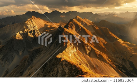 Golden sunlight illuminates jagged mountains, casting shadows and highlighting the rugged, stunning view. 116923304