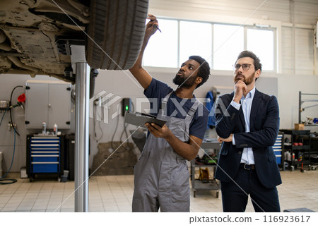 Mechanic and customer inspecting car in auto repair shop 116923617