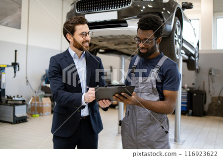 Mechanic and businessman discussing car maintenance in garage Mechanic and businessman discussing car maintenance in garage 116923622