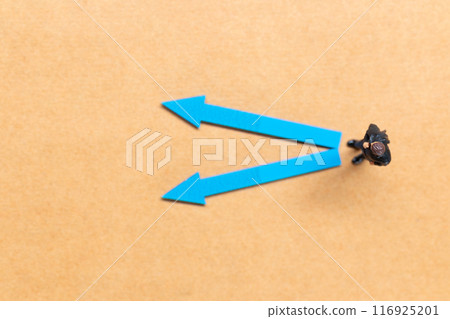 A miniature people stands at the intersection of colorful arrows on a light brown background A miniature people stands at the intersection of colorful arrows on a light brown background 116925201