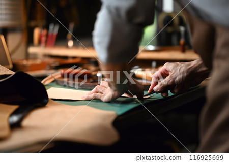 Close up view of craftsman skillfully using a cutting tool to shape the leather 116925699