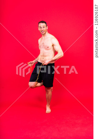 Fit man jumping with skipping rope. Isolated on red studio background 116926187
