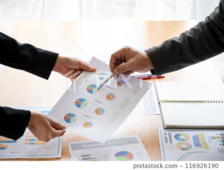 Business professionals reviewing financial charts and graphs, focusing on a detailed report with pie charts, emphasizing data analysis, strategy planning, and corporate teamwork 116926190