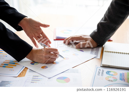 Business professionals analyzing financial reports and charts, focusing on detailed discussions with data and documents, emphasizing strategy, collaboration, and corporate planning 116926191