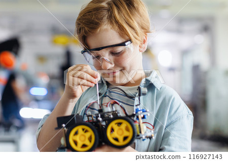 Portrait of schoolboy building robotic car in after-school robotics club. Children learning robotics in Elementary school. Science for kids. Portrait of schoolboy building robotic car in after-school robotics club. Children learning robotics in Elementary school. Science for kids. 116927143