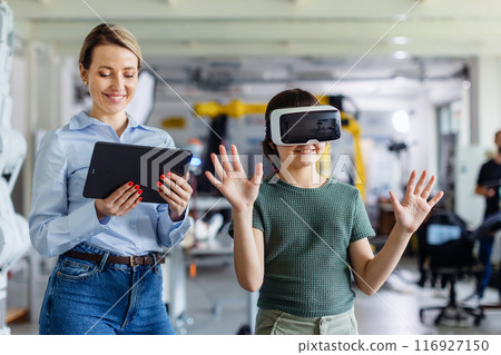Schoolgirl learning with VR headset on head. Teacher using modern technology, virtual reality during class, lesson. 116927150