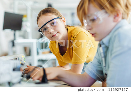 Two classmates working together on circuit board, building robot in after-school robotics club. Children learning robotics in Elementary school. 116927157