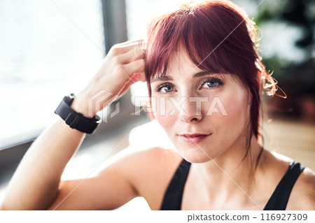 Headshot of beautiful redhead woman during fitness routine. Home workout on gym mt in living room, sporty woman wearing sportswear. 116927309