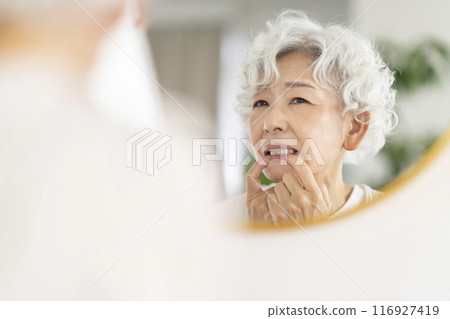 Senior woman concerned about her gums while looking in the mirror 116927419