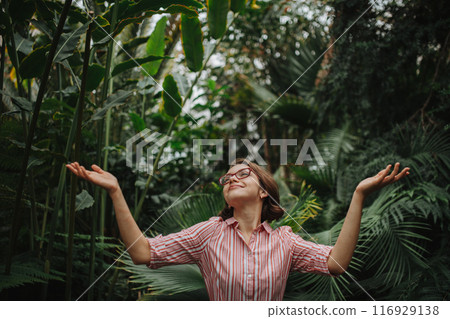 Beautiful woman standing in botanical garden, in the middle of lush green foliage, arms open. Beautiful woman standing in botanical garden, in the middle of lush green foliage, arms open. 116929138