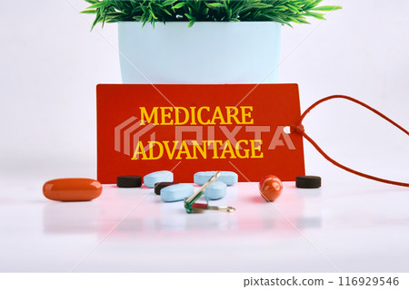 Medicare Advantage text on a red card, with pills, vitamins in the foreground on a white background 116929546