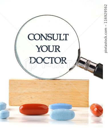 Medical concept.The inscription Consult your doctor through a magnifying glass on a wooden block in front of a white background, a vertical photo 116929562