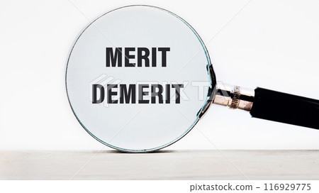 Merit, demerit and its retributions at the level of the individual. MERIT DEMERIT words through a magnifying glass on a light gray background 116929775
