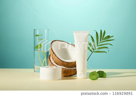 Creative template for advertising pic was taken over blue background from front angle . An unlabeled cosmetic tube and jar, coconut and centella asiatica ingredients placed in back Creative template for advertising pic was taken over blue background from front angle . An unlabeled cosmetic tube and jar, coconut and centella asiatica ingredients placed in back 116929891