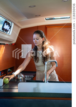 Young woman standing with green apple in kitchen in cabin of modern yacht during sailing in sea. Yacht life concept Young woman standing with green apple in kitchen in cabin of modern yacht during sailing in sea. Yacht life concept 116930436