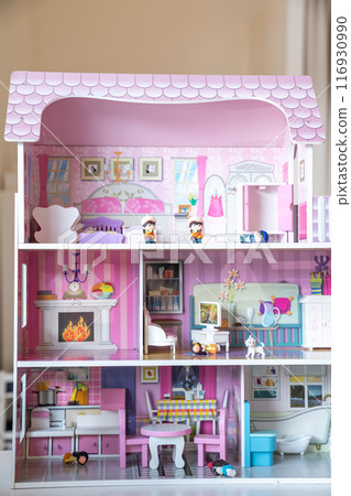 The photo of huge pink dollhouse model furnished with miniature furniture in a kids room. The photo of huge pink dollhouse model furnished with miniature furniture in a kids room. 116930990