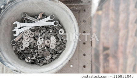 A bucket full of wrenches, washers and stud bolts is placed on the scaffolding. 116931043