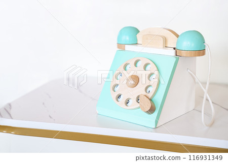 An antique blue turquoise and white rotary home phone toy made of wood rests on a white marble patterned shelf for Kid learning and play. 116931349