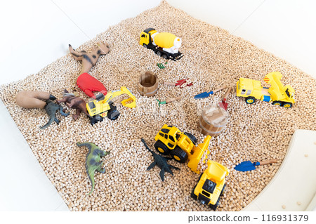 Yellow construction toy vehicles and Dinosaurs Toys are placed in kid playground filled with wooden cubes around it. 116931379