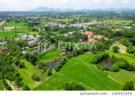 Drone view of Sufficiency Economy, Land full of agricultural activities with green rice fields, big ponds, and trees. Small houses and temple close by a pond. Drone view of Sufficiency Economy, Land full of agricultural activities with green rice fields, big ponds, and trees. Small houses and temple close by a pond. 116931429