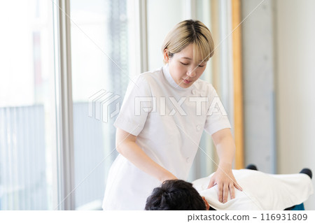 一位年輕的金髮短髮女脊椎按摩師，穿著凱西白大褂進行治療（自由髮色，按照自己的方式工作，工作環境） 116931809