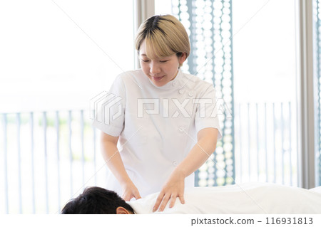 一位年輕的金髮短髮女脊椎按摩師，穿著凱西白大褂進行治療（自由髮色，按照自己的方式工作，工作環境） 116931813