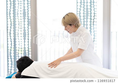 一位年輕的金髮短髮女脊椎按摩師，穿著凱西白大褂進行治療（自由髮色，按照自己的方式工作，工作環境） 116931817