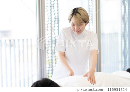 一位年輕的金髮短髮女脊椎按摩師，穿著凱西白大褂進行治療（自由髮色，按照自己的方式工作，工作環境） 116931824