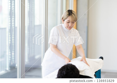 一位年輕的金髮短髮女脊椎按摩師，穿著凱西白大褂進行治療（自由髮色，按照自己的方式工作，工作環境） 116931829
