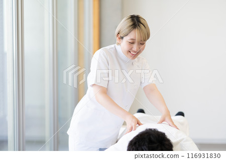 一位年輕的金髮短髮女脊椎按摩師，穿著凱西白大褂進行治療（自由髮色，按照自己的方式工作，工作環境） 116931830