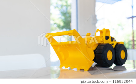 A yellow construction Loader toy vehicle with articulated parts built with sturdy plastic is placed on a table. A yellow construction Loader toy vehicle with articulated parts built with sturdy plastic is placed on a table. 116932044