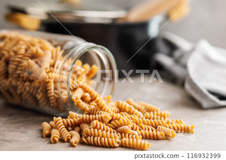 Uncooked whole grain pasta. Raw fusilli in jar on kitchen table. 116932399
