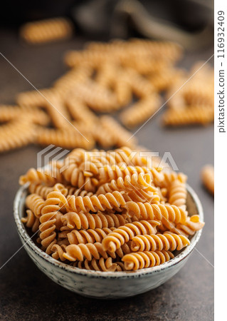 Uncooked whole grain pasta. Fusilli pasta in bowl on black kitchen table. 116932409
