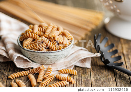 Uncooked whole grain pasta. Raw fusilli pasta in bowl on wooden table. 116932416