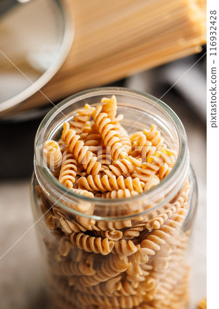 Uncooked whole grain pasta. Raw fusilli in jar on kitchen table. Uncooked whole grain pasta. Raw fusilli in jar on kitchen table. 116932428