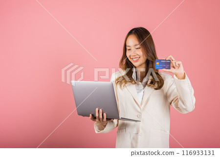 Portrait of Asian beautiful young woman customer showing credit card for online payment shopping transactions cashback loan on laptop studio shot isolated on pink background 116933131