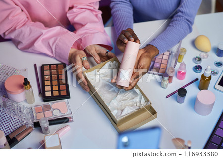 Top view closeup of two young women reviewing skincare and make up products and holding pink moisturizing cream, copy space Top view closeup of two young women reviewing skincare and make up products and holding pink moisturizing cream, copy space 116933380