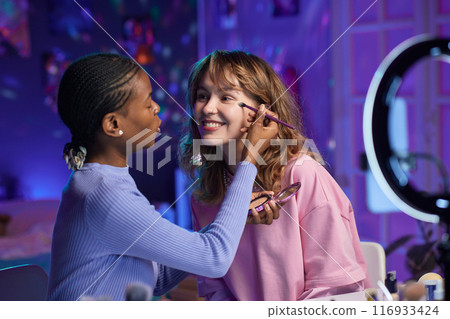 Portrait of two young women testing make up products and recording video with ring light for social media Portrait of two young women testing make up products and recording video with ring light for social media 116933424