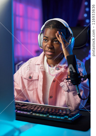 Vertical portrait of troubled African American girl playing difficult video game online and wearing headphones 116933636